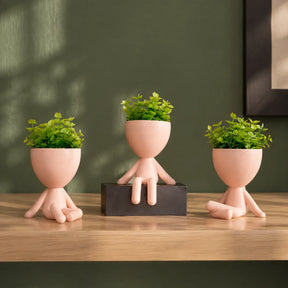Três mini vasos rosa-claro com plantas artificiais sobre aparador